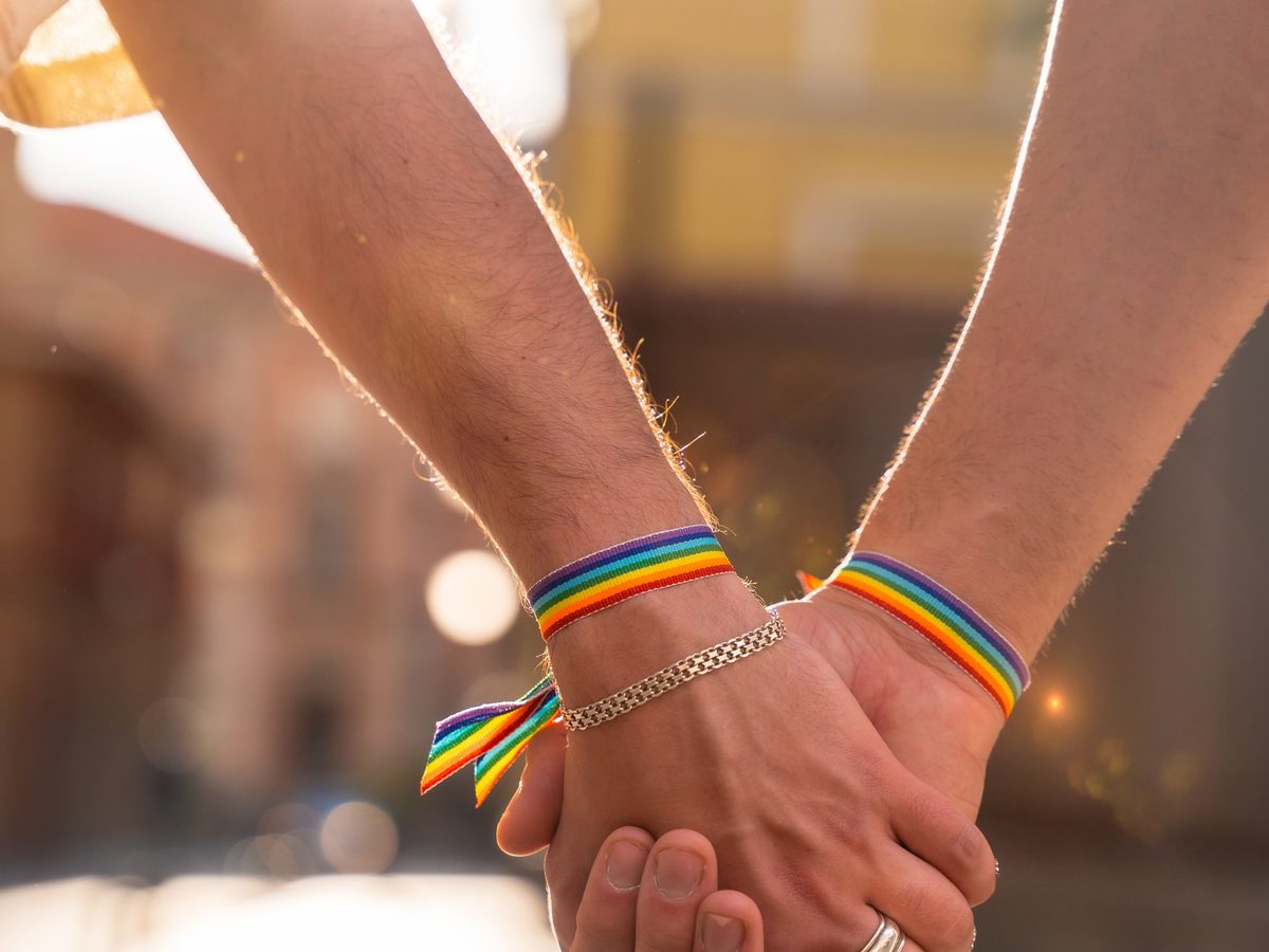 Two people holding hands with a rainbow flag